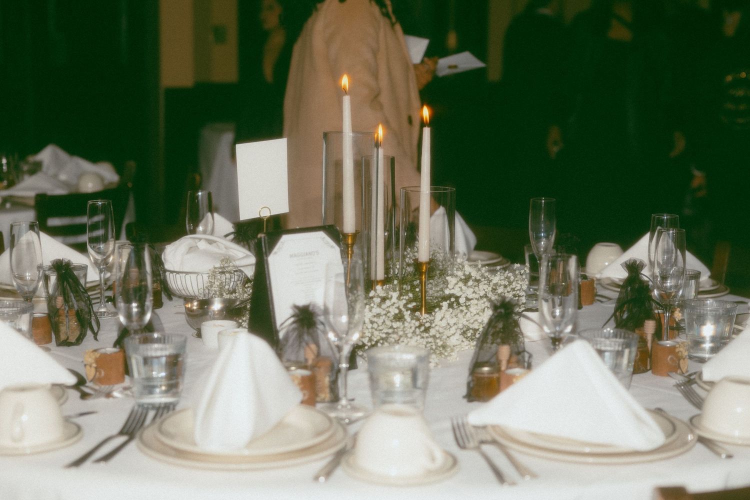 Elegantly set wedding reception table with white napkins, candles, glassware, and baby's breath floral centerpieces.