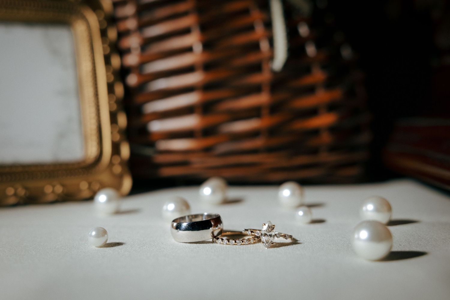 Wedding rings and pearl jewelry arranged on white surface with wicker basket background.