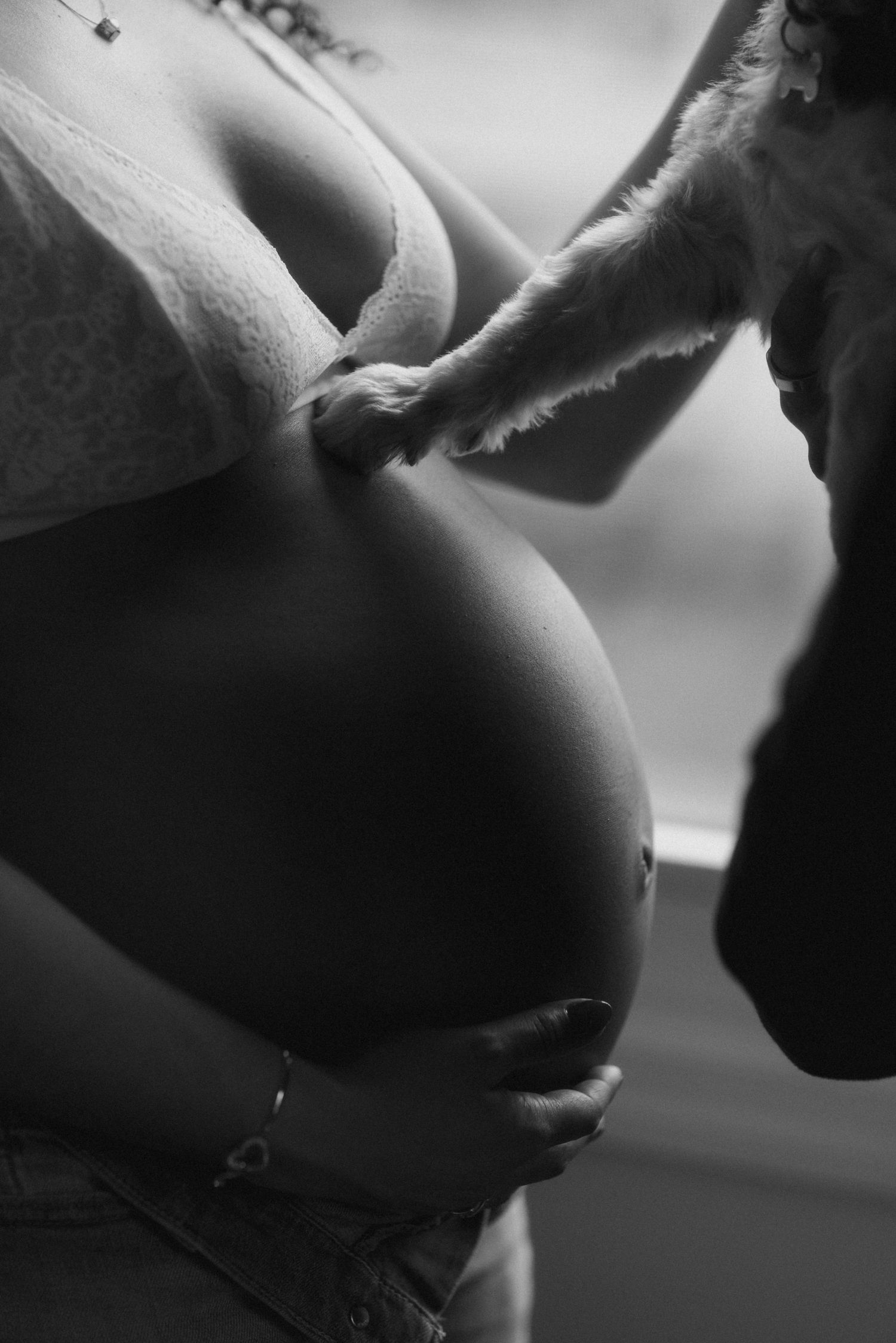 Black and white close-up of pregnant woman's baby bump with partner leaning in to kiss it tenderly.