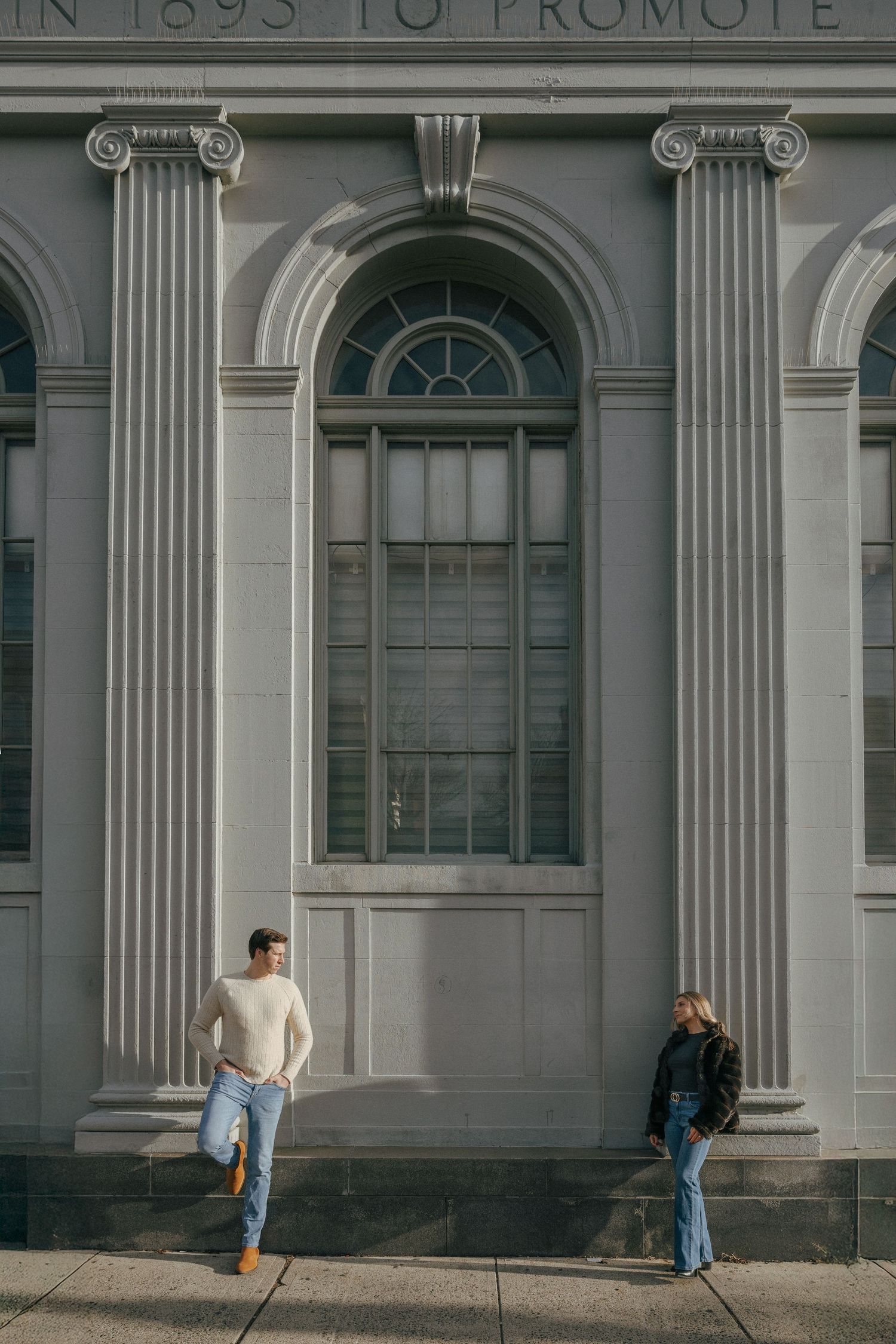 Couple leaning against a grand neoclassical building facade with arched windows and columns.
