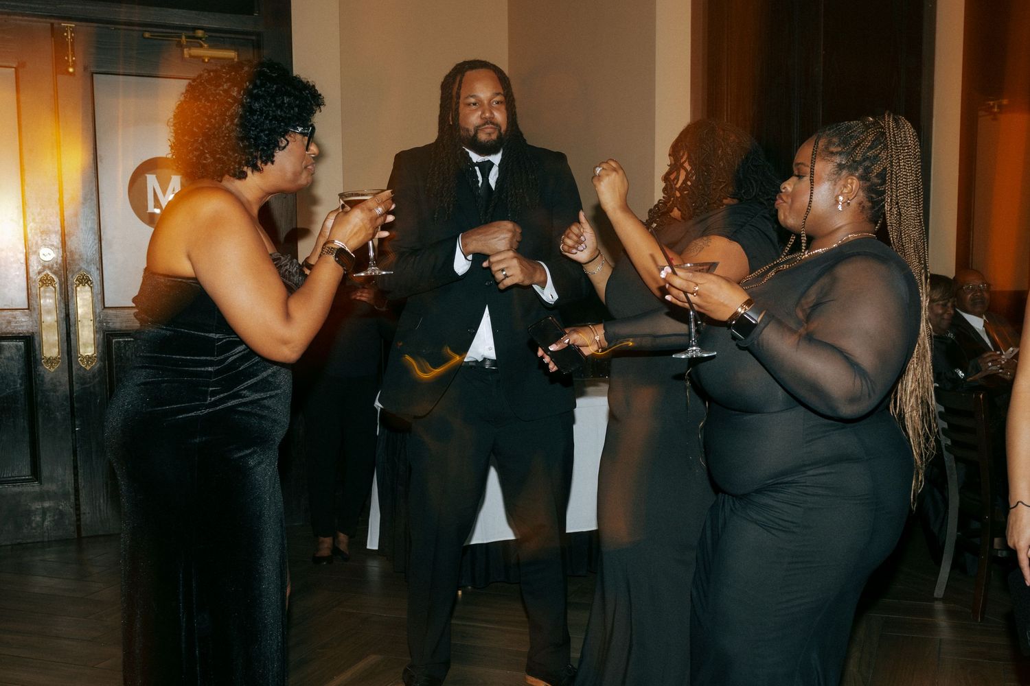 Guests in formal black attire dancing and celebrating energetically at a wedding reception party.