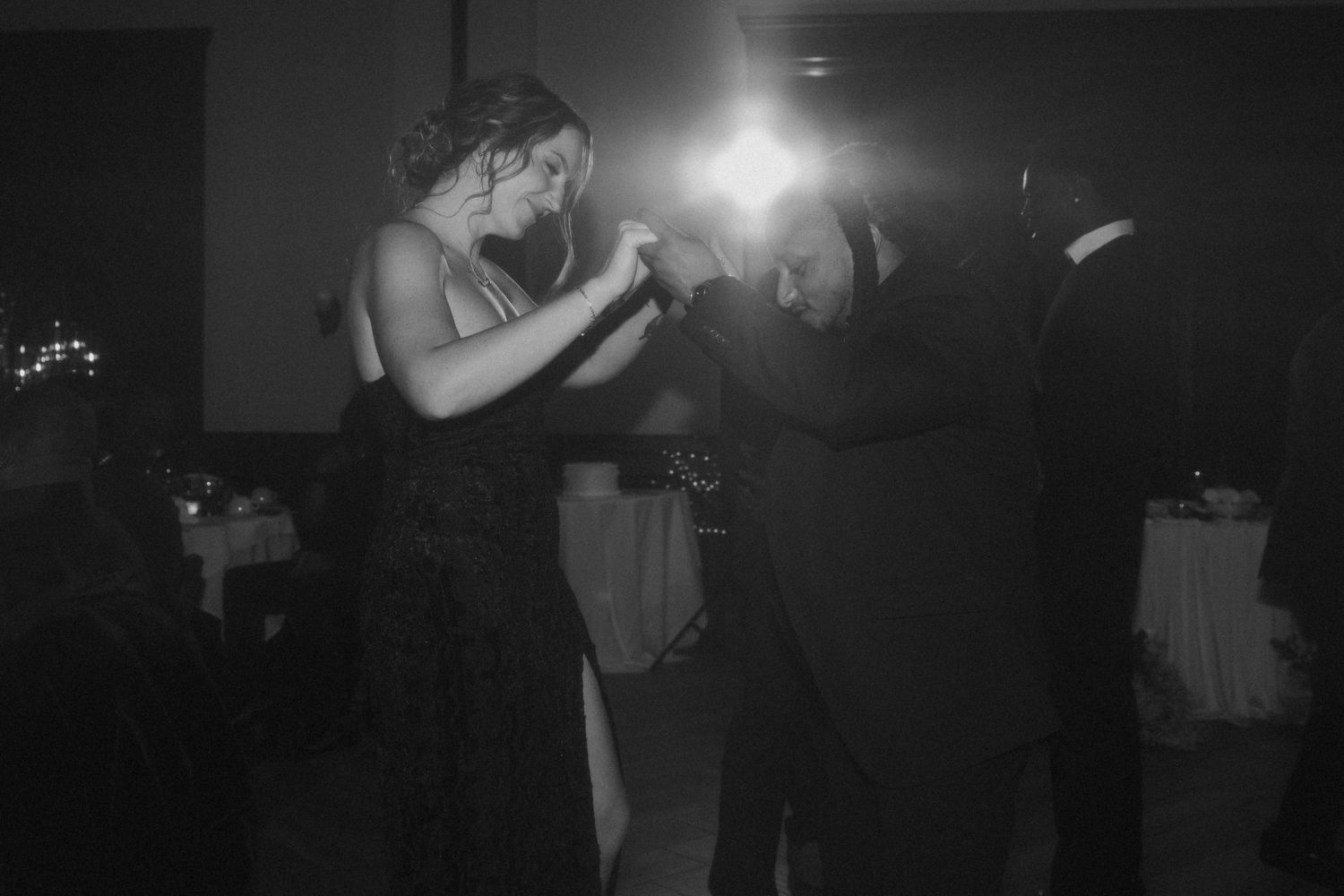 Black and white photo of a couple sharing an intimate slow dance together at a dimly lit wedding reception.