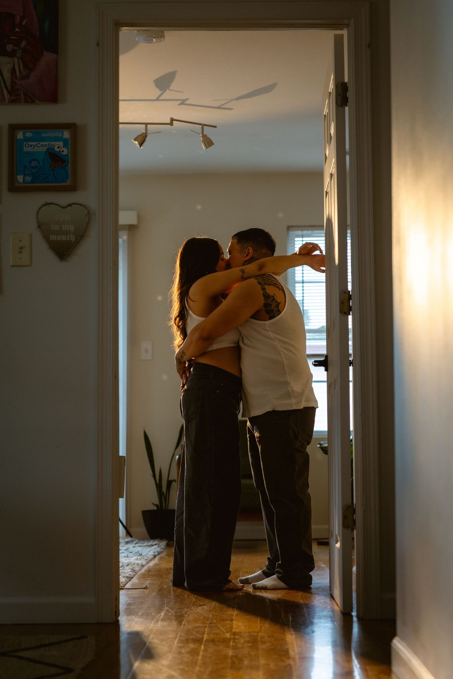 Couple sharing a romantic embrace and kiss in a warmly lit home interior viewed through a doorway.