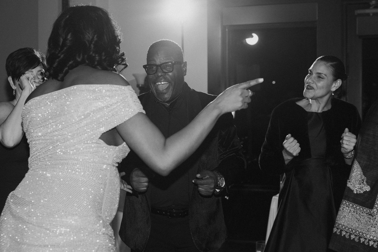 Black and white photo of guests dancing and laughing joyfully at a lively wedding reception celebration.