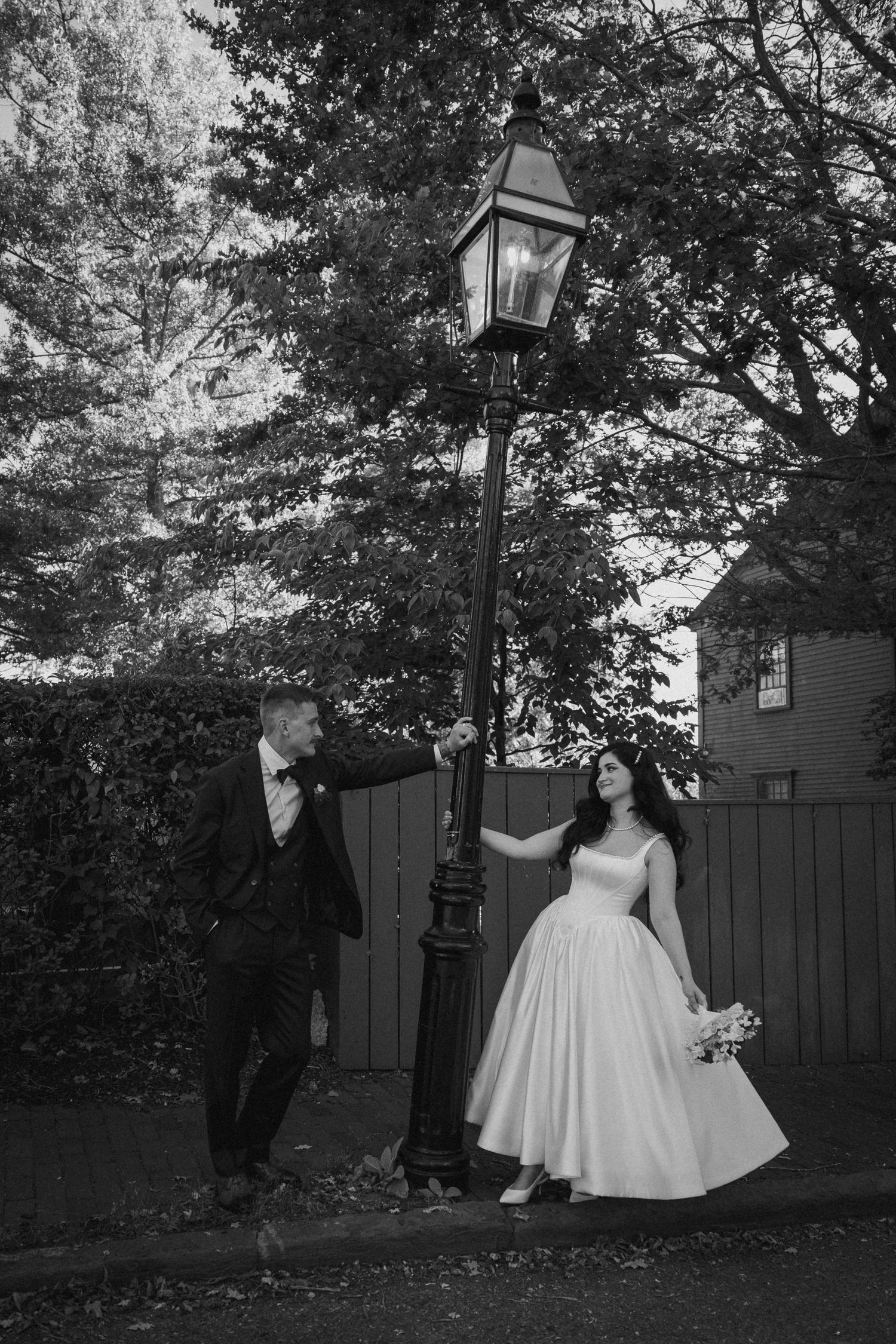 Bride and groom pose by vintage lamppost in black and white outdoor wedding portrait.