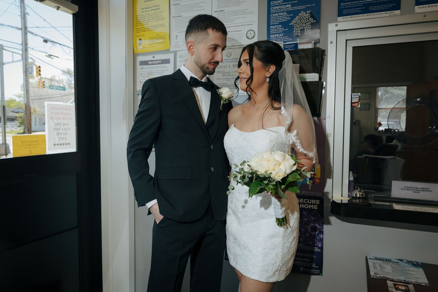 Bride and groom in elegant wedding attire, she holds white bouquet, standing together in a doorway.