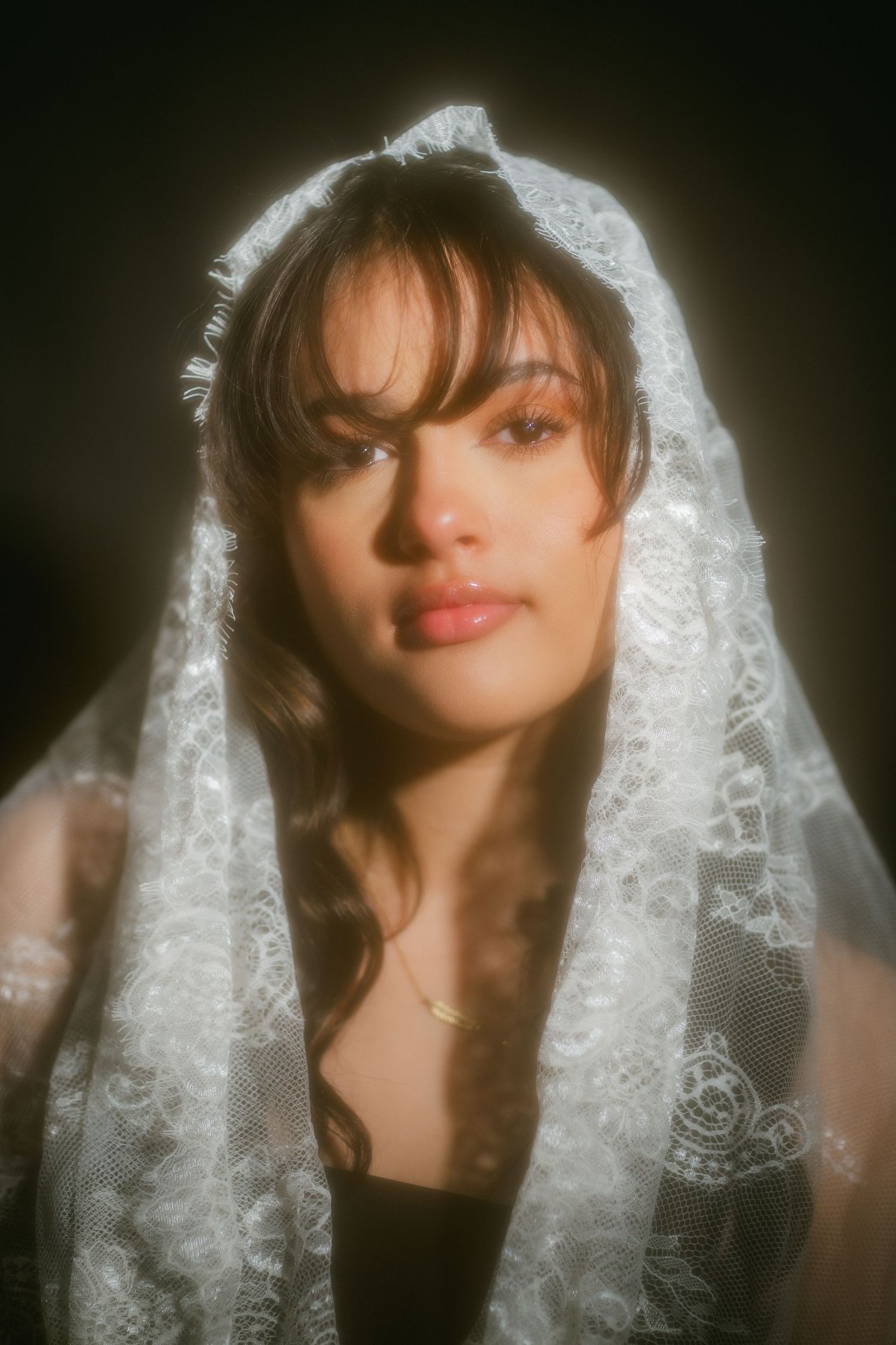 Close portrait of woman wearing white lace mantilla veil on dark background.