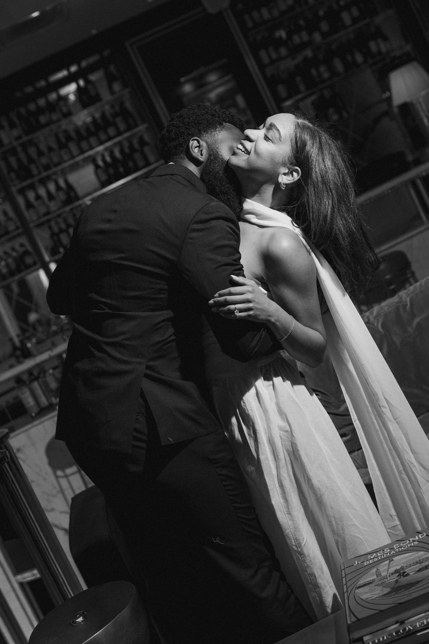 Couple shares a romantic kiss in a dimly lit restaurant, groom in suit and bride in white gown.