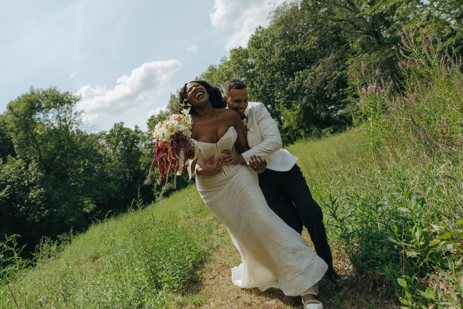 Joyful bride and groom dancing on a lush green hillside on their wedding day.