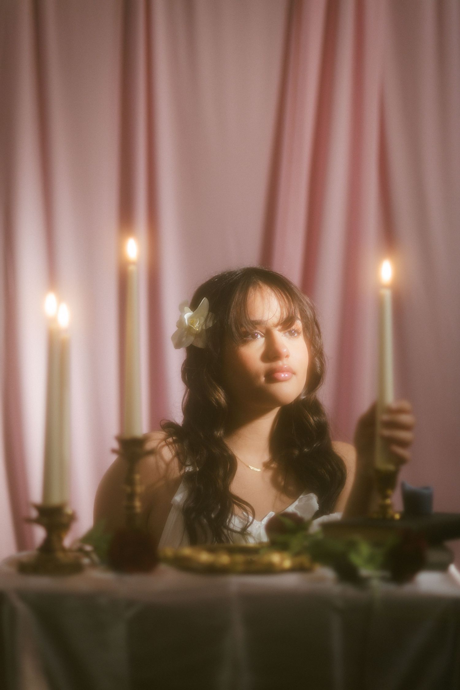 Woman with flower in hair holding candle at romantic table with roses and pink curtain background.