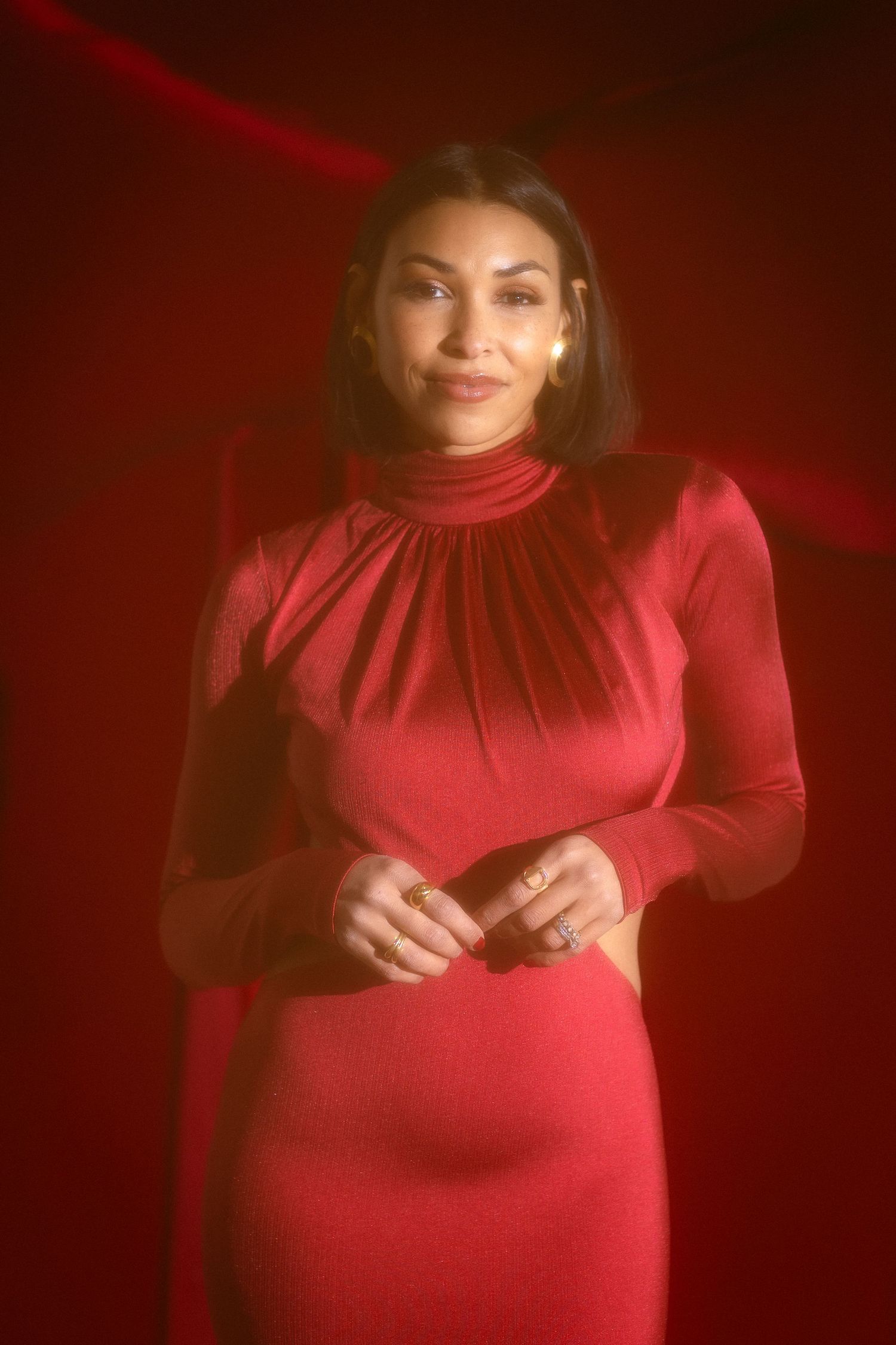Woman in elegant red turtleneck dress posing against rich red backdrop.