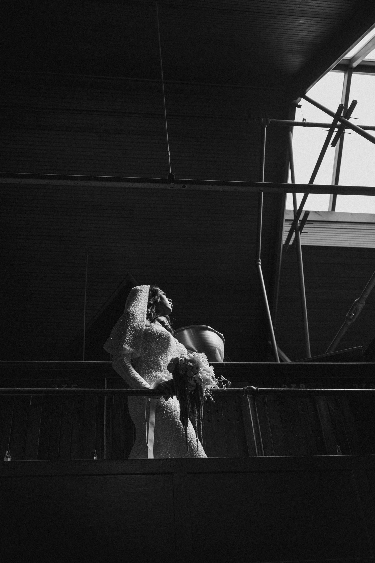 Black and white silhouette of bride in veil on industrial venue balcony.