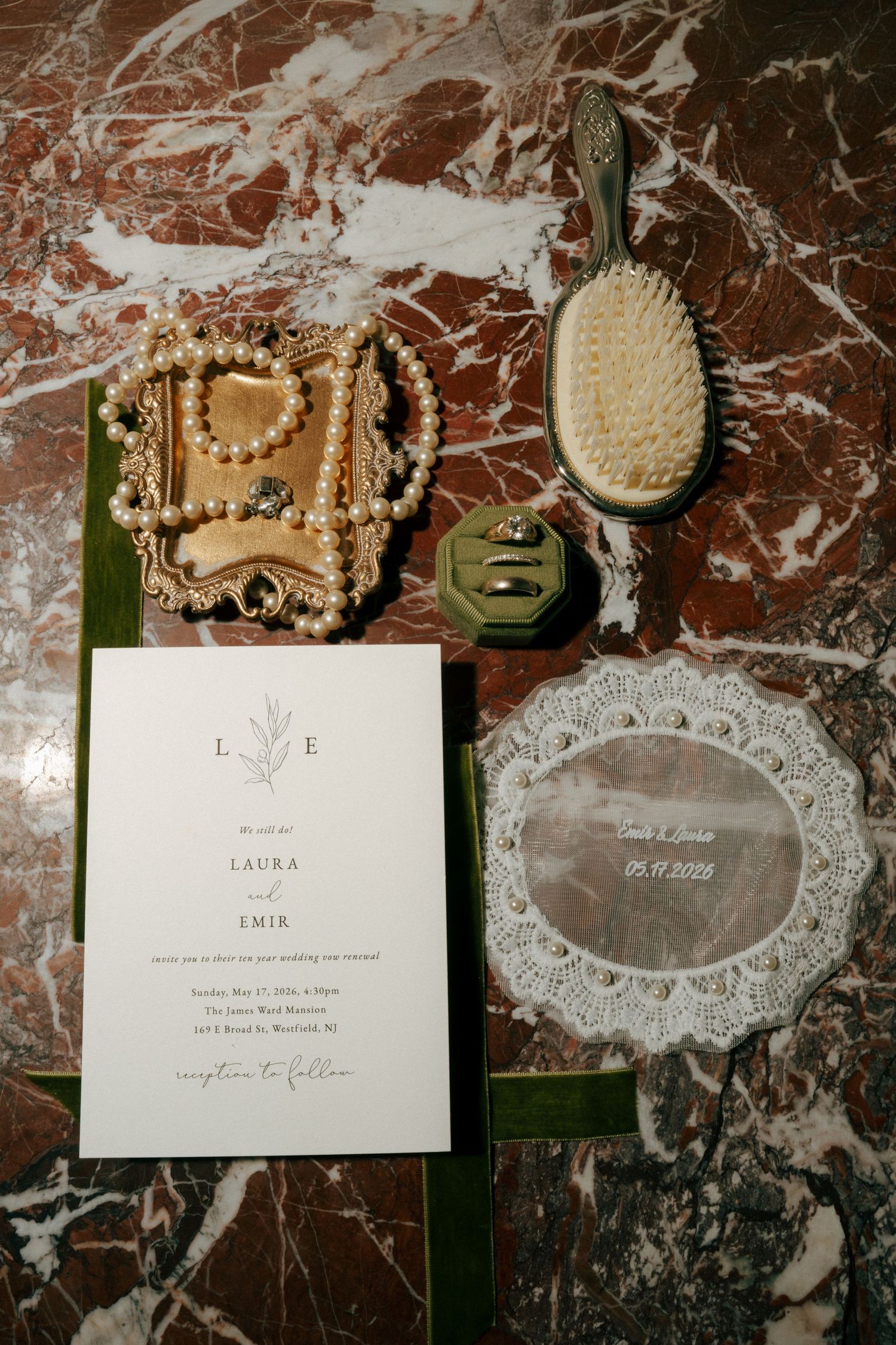 Wedding invitation suite for Laura and Emir displayed on marble with pearl jewelry, vintage hair brush, and green velvet ring box.