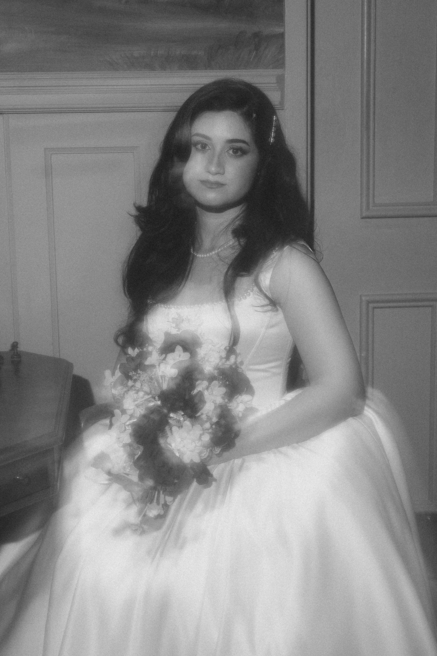 Black and white portrait of bride in elegant white ball gown holding floral bouquet in classic interior.