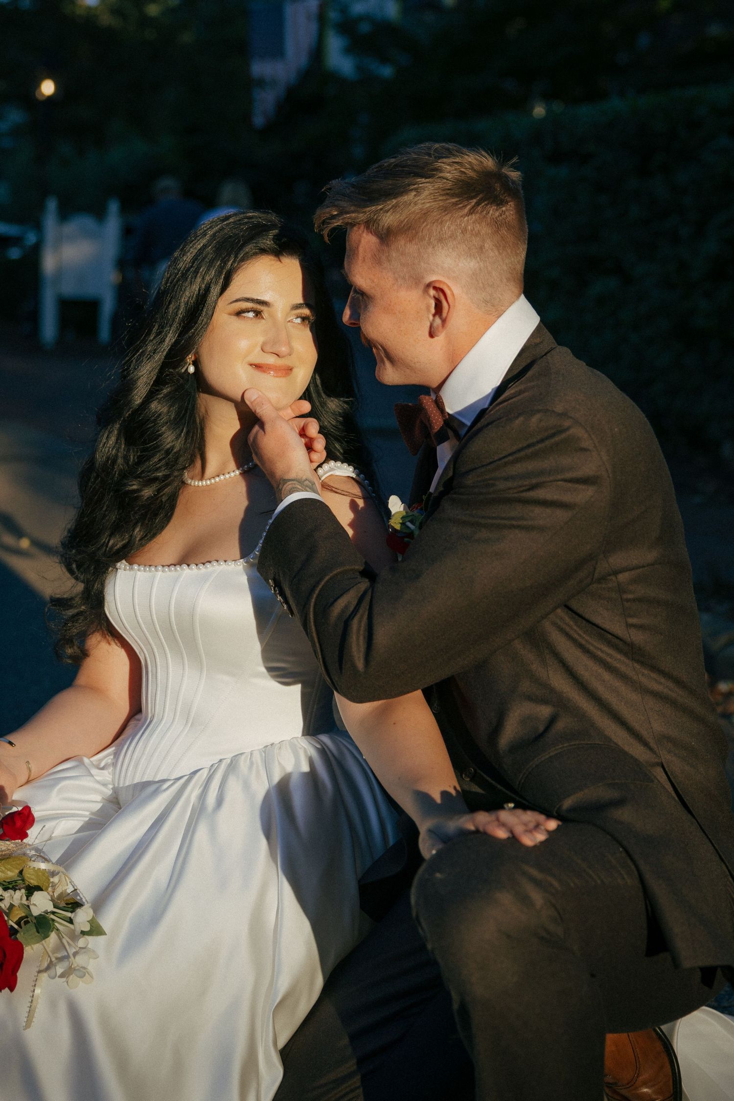 Groom tenderly touches bride's face as they share a romantic moment outdoors at dusk.