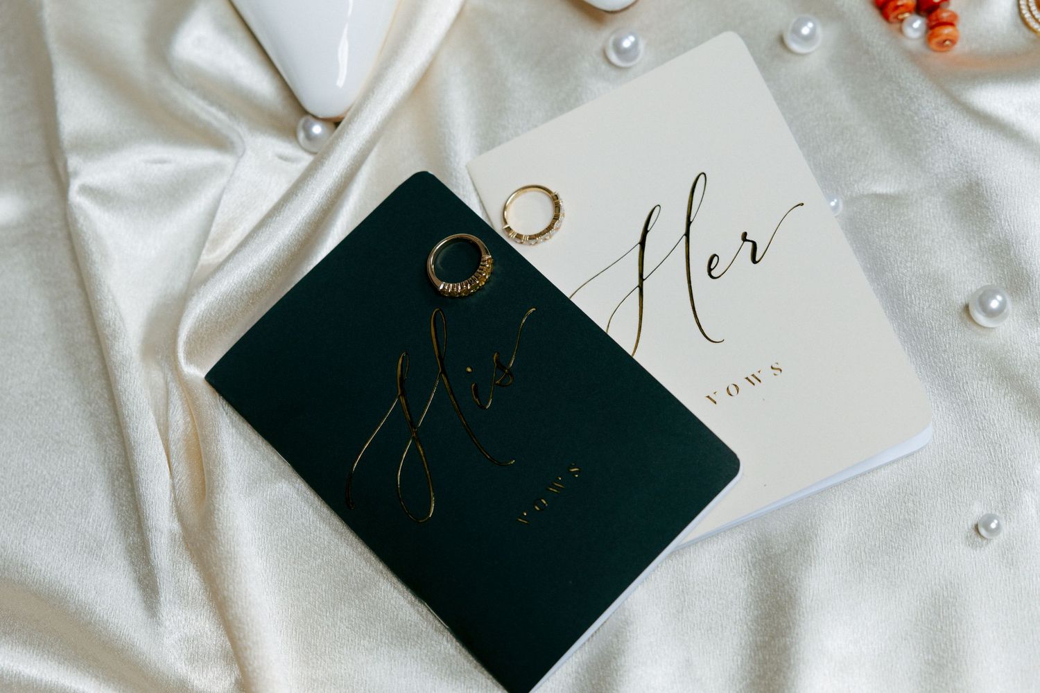 His and hers wedding vow books with gold rings on white satin fabric.