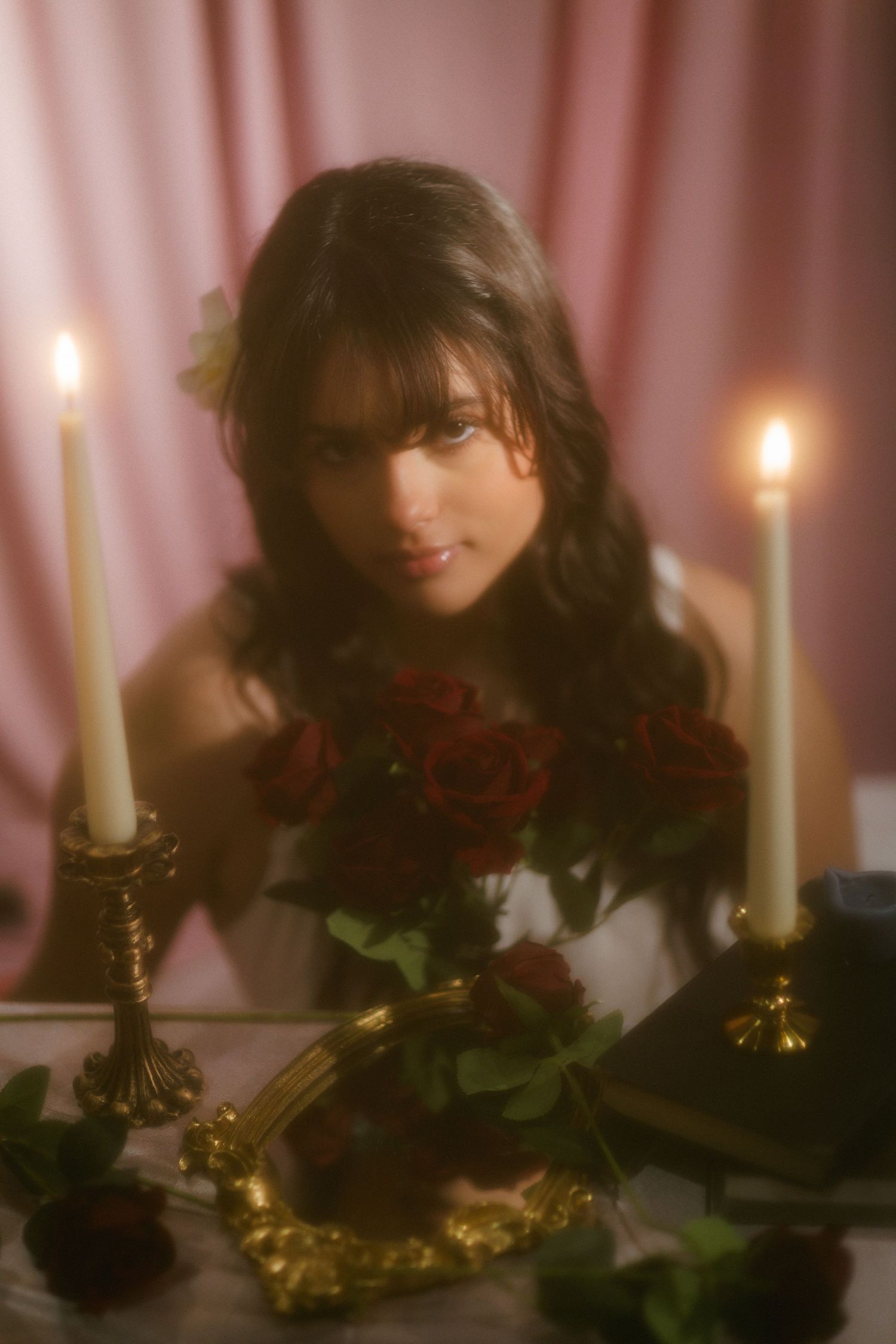 Woman with floral hair accessory looking at camera at romantic candlelit table with red roses.