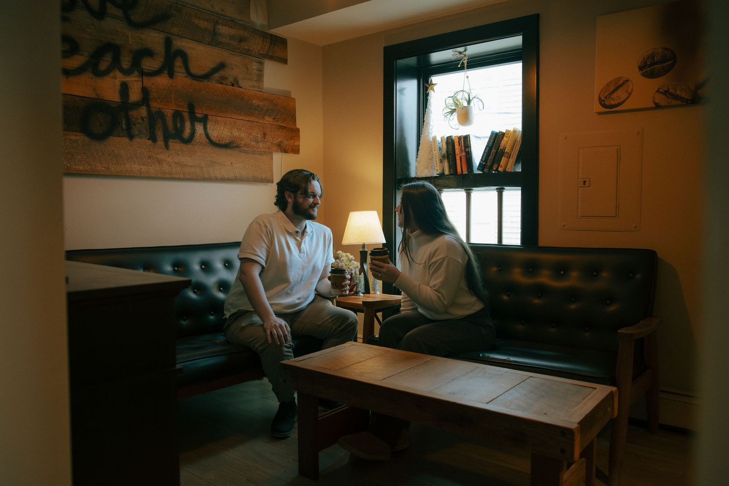 Two people sit facing each other on leather sofas in a cozy, warmly lit lounge with wooden decor.