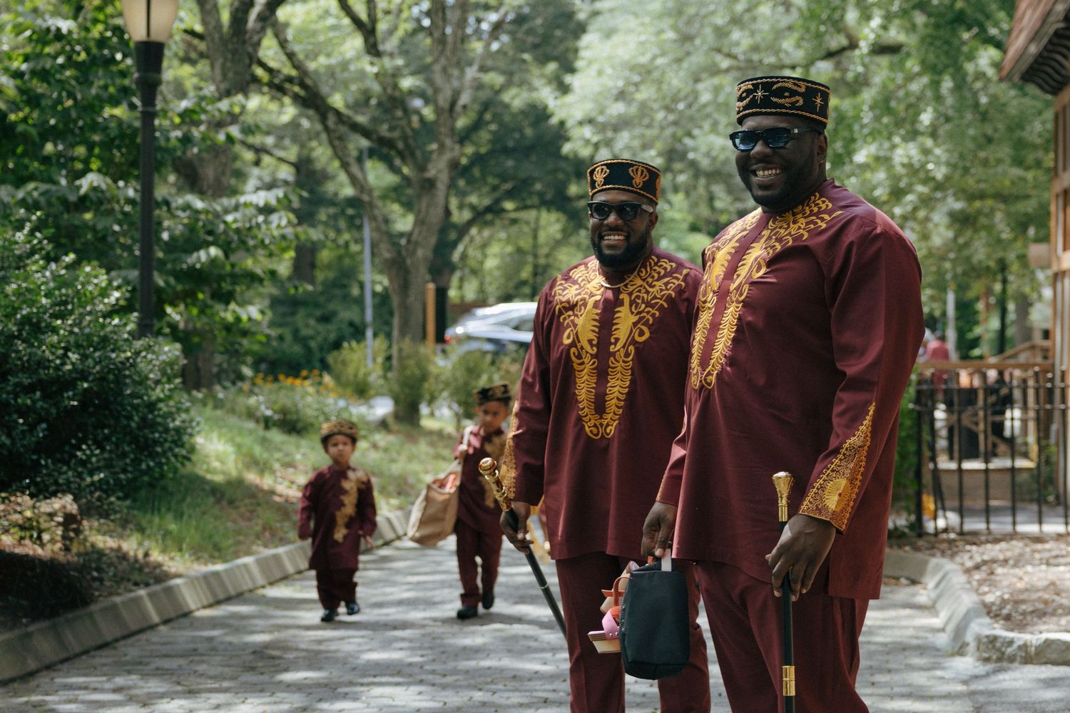 Three people in matching maroon and gold African attire walk along a tree-lined path.