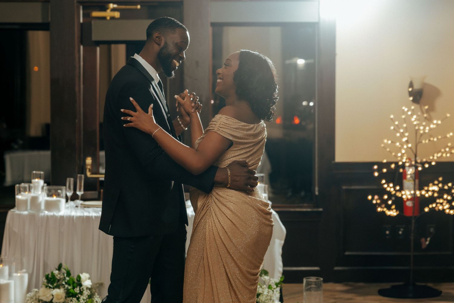 Elegant couple sharing first dance at wedding reception in dimly lit ballroom with candles and fairy lights.