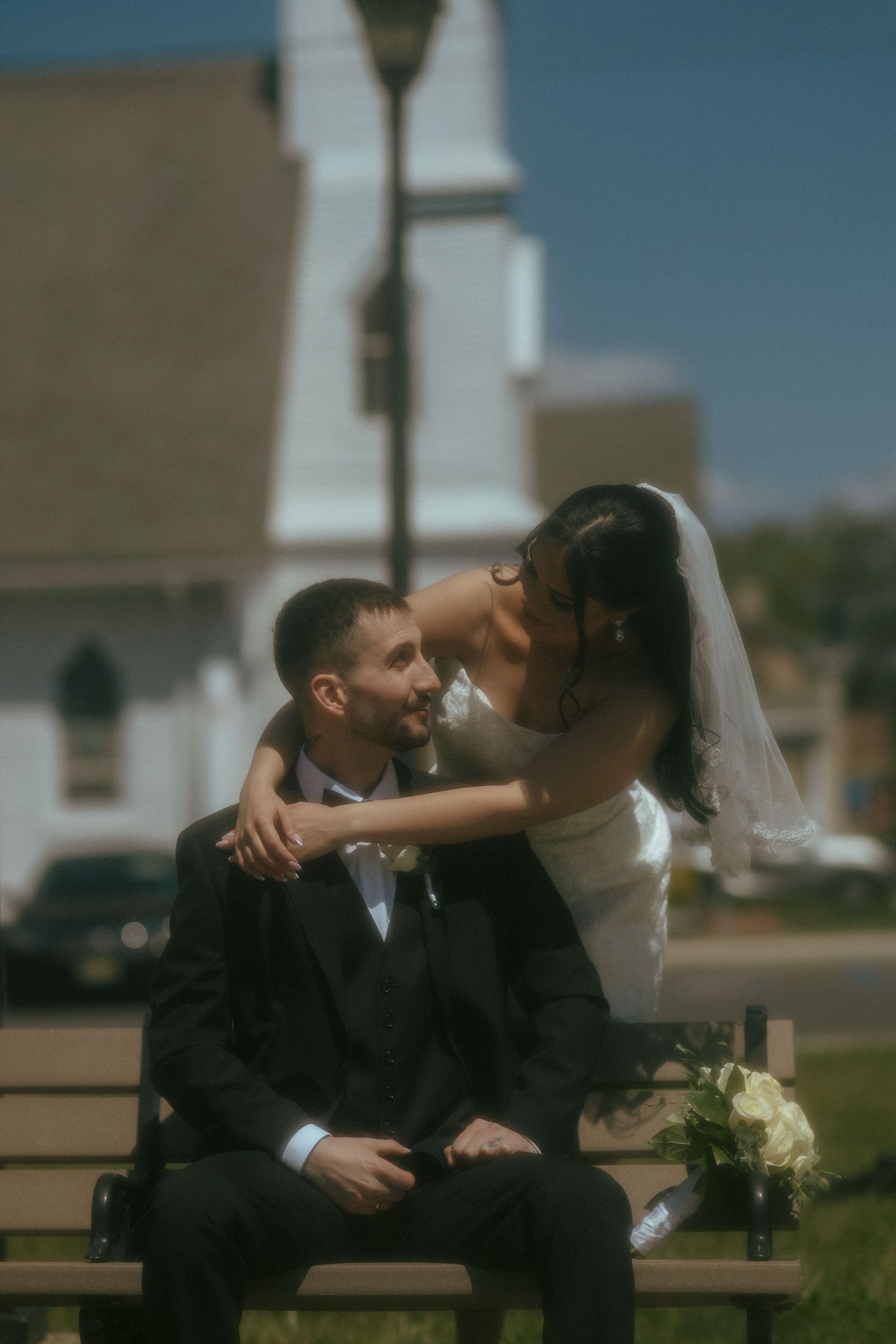 Bride and groom share a romantic moment on a bench outside a white church on their wedding day.