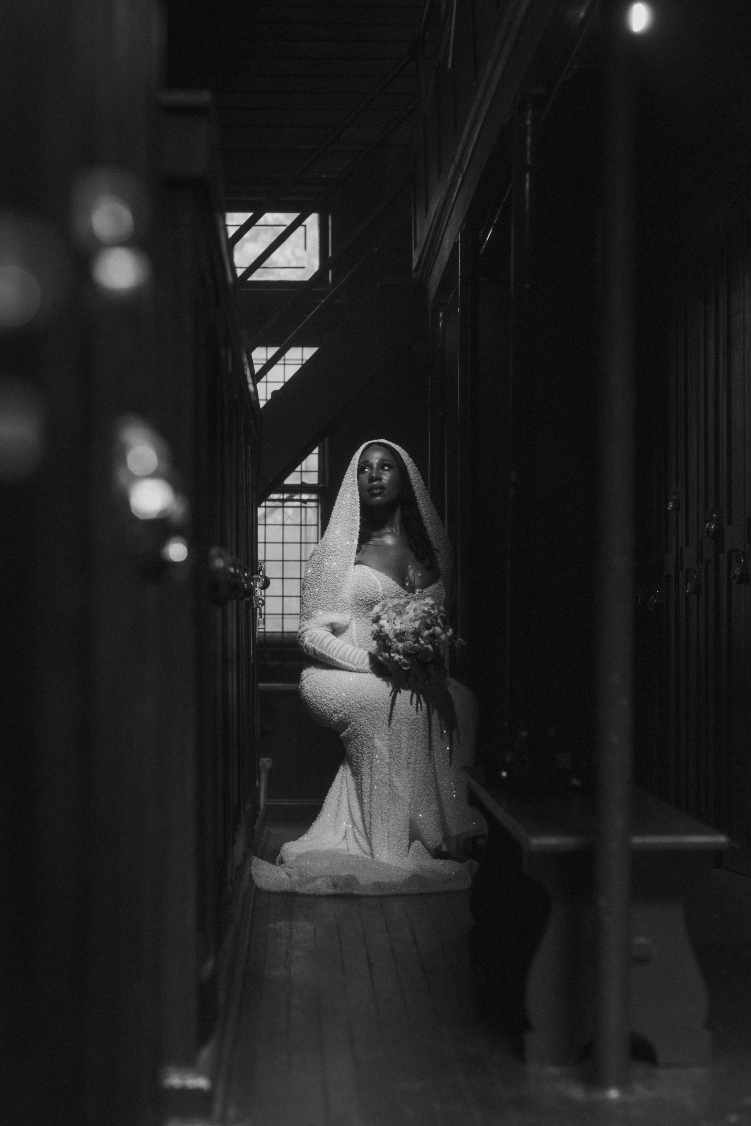 A bride in a white gown and veil holds a bouquet in a dramatic black and white photo.