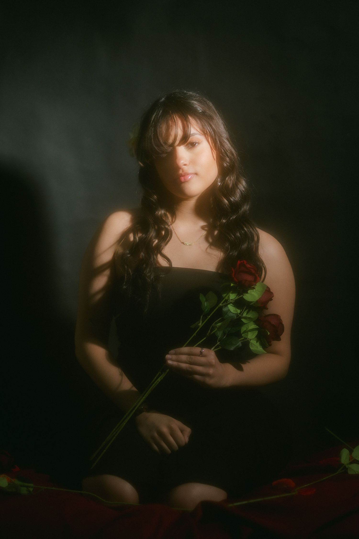 Woman in black dress holding red roses against dark dramatic studio background.