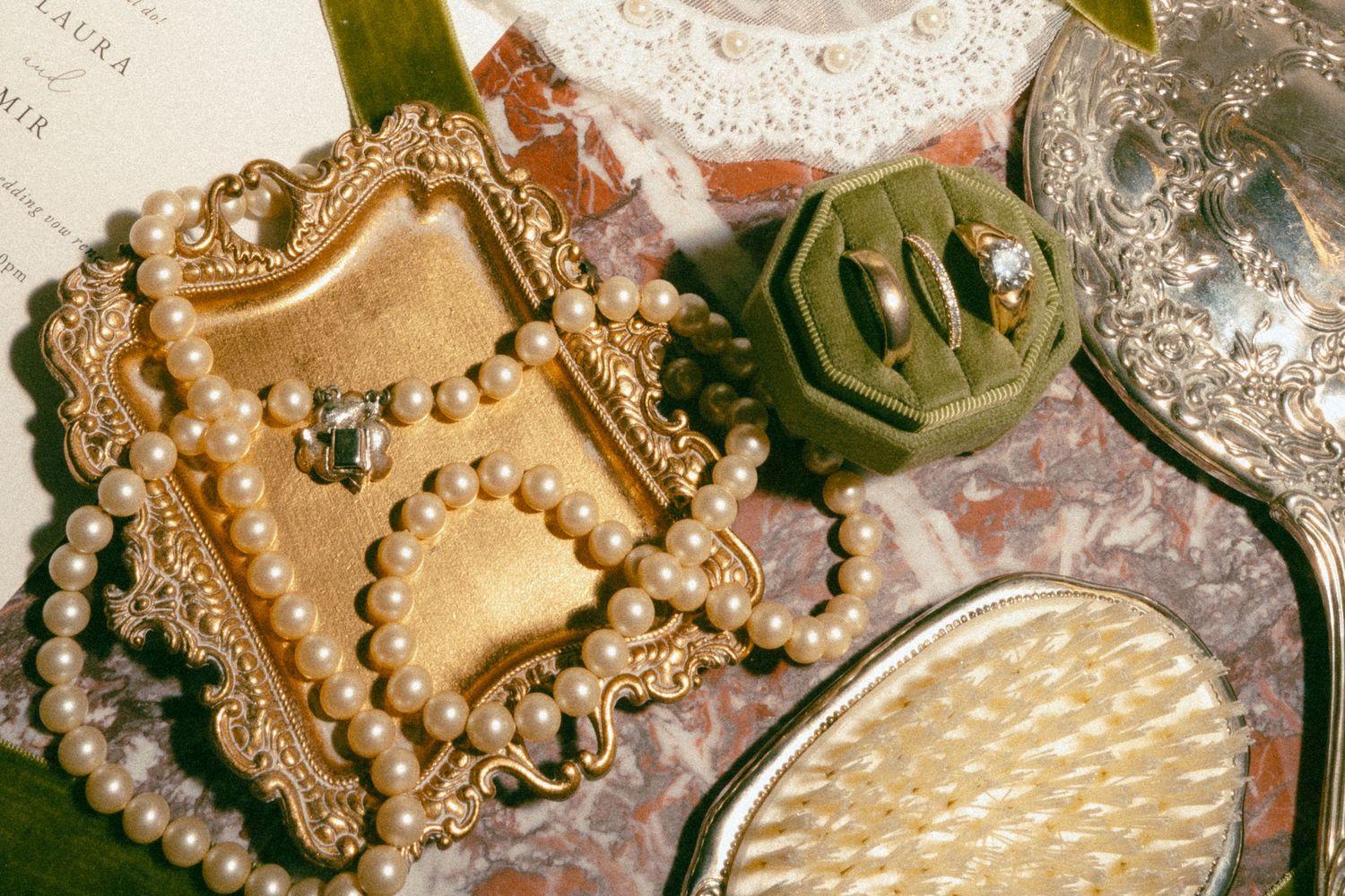 Vintage gold jewelry box with pearl necklace, velvet ring holder, and silver compact mirror on marble surface.