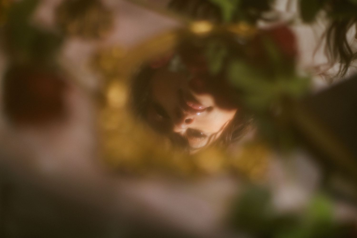 Dreamy blurred portrait of a woman framed by lush green leaves and golden bokeh light.