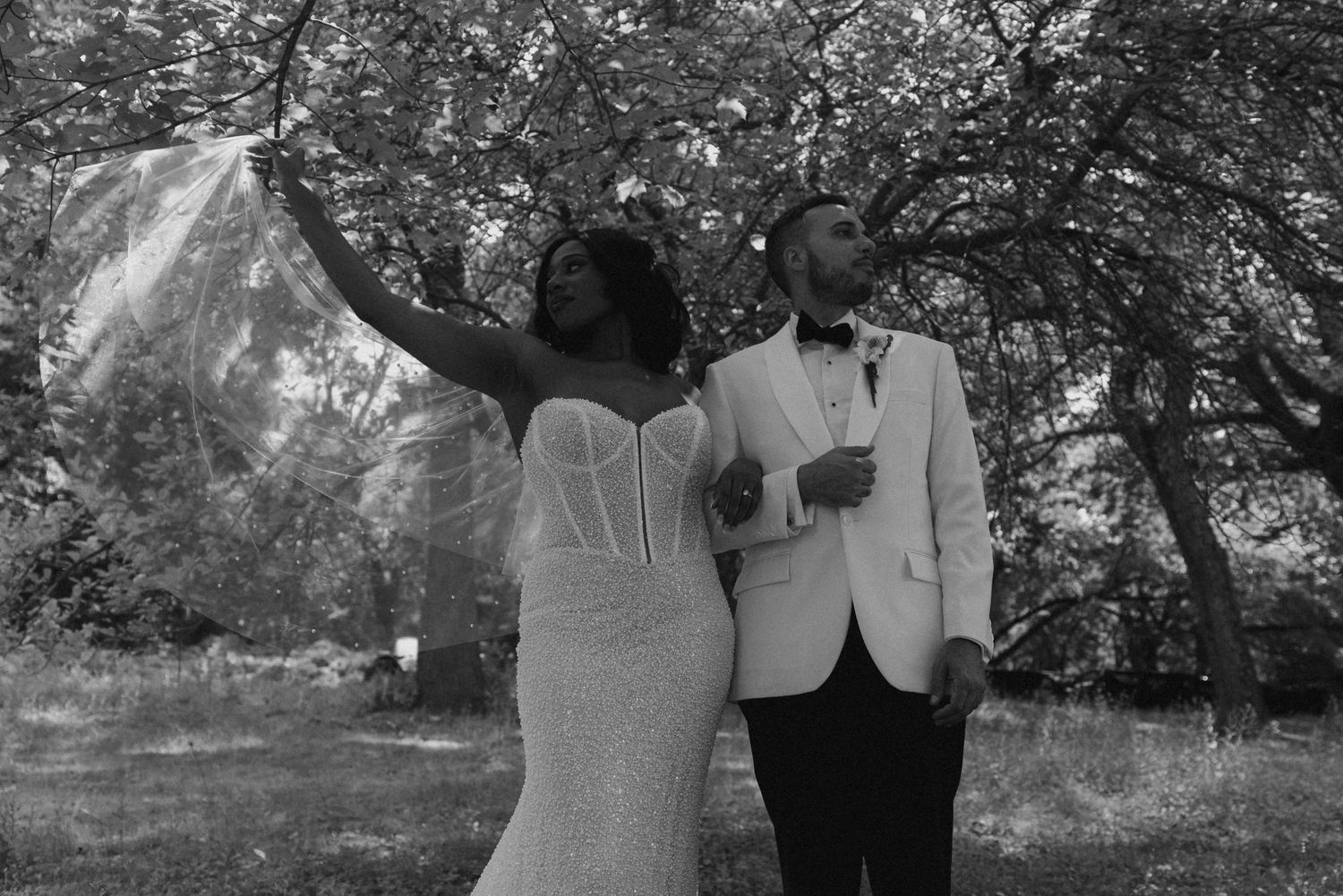 Black and white photo of bride tossing veil with groom in white tuxedo.