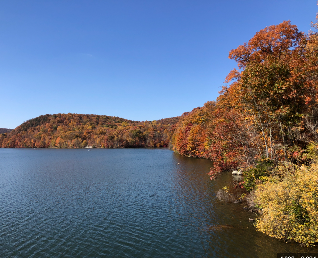 Serene autumn lake surrounded by vibrant fall foliage in red, orange, and yellow under a clear blue sky.