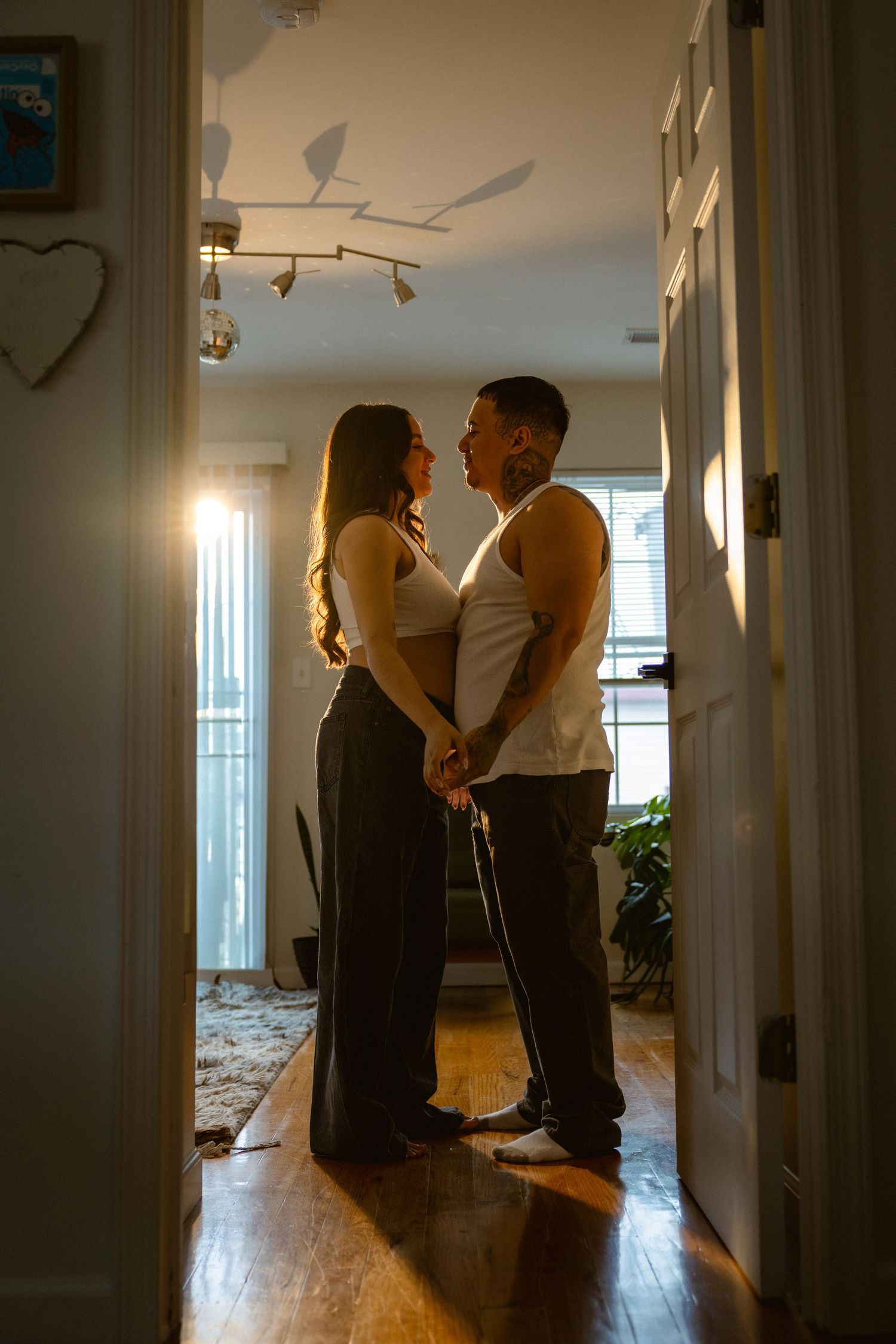 Couple holding hands in warm backlit home interior, standing together in a doorway with hardwood floors.
