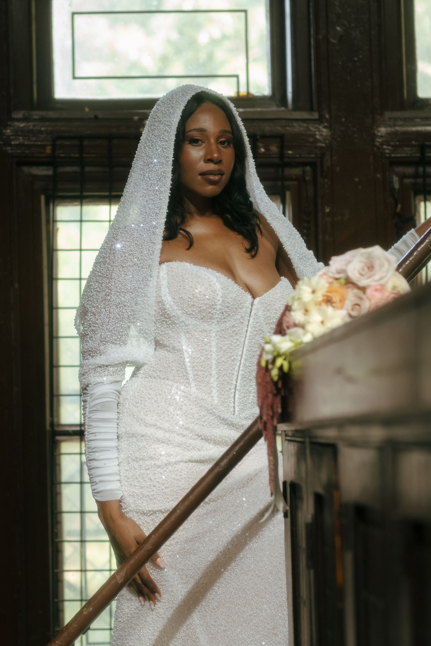Bride in sparkly white gown and veil posing on staircase with floral bouquet.