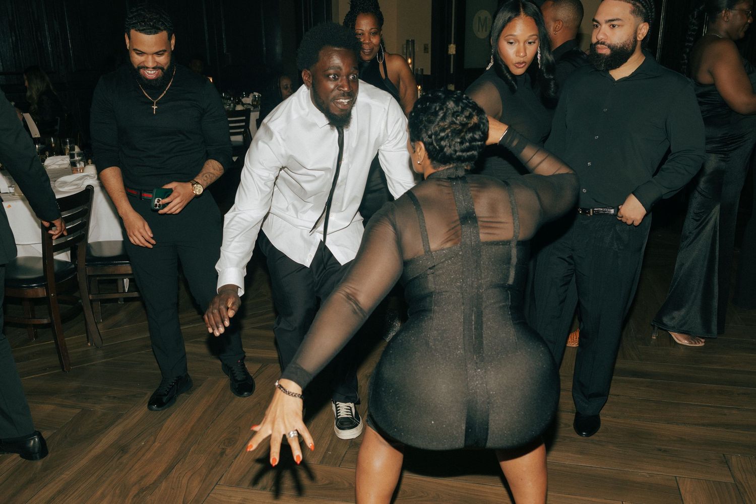 People dancing energetically at an indoor party event, dressed in black and white formal attire.