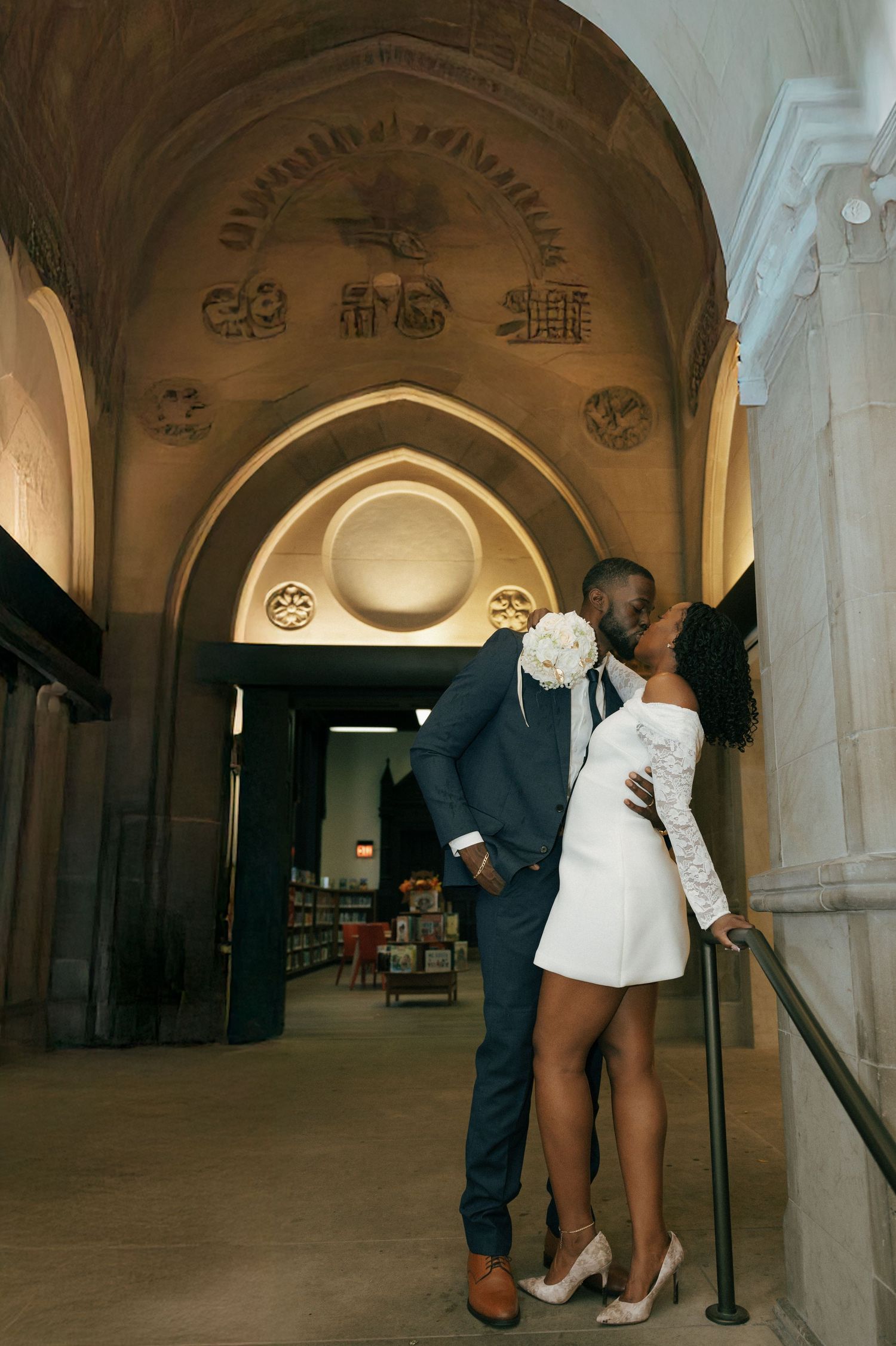 Black bride and groom sharing a kiss under ornate cathedral archway during wedding celebration.