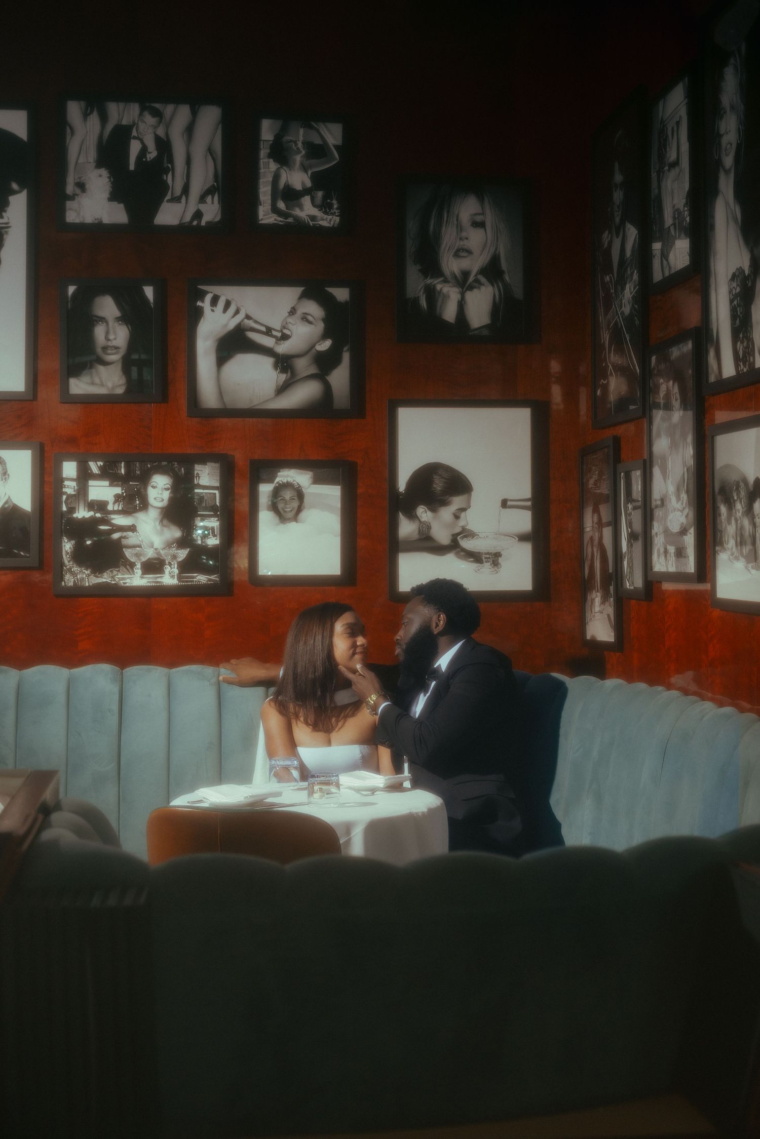 Couple sharing an intimate dinner at a romantic restaurant booth surrounded by black and white celebrity photos on red walls.