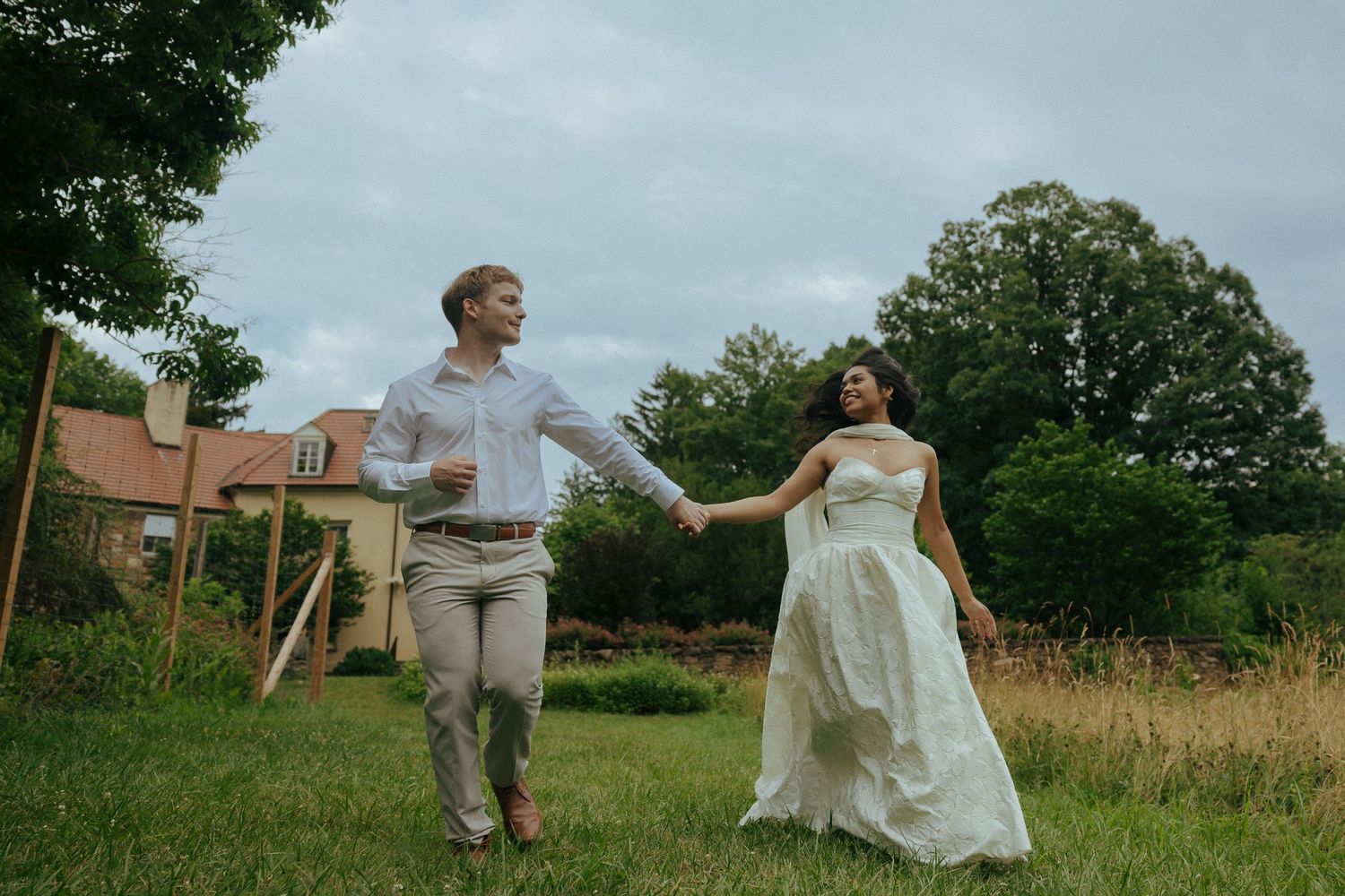 A joyful bride and groom hold hands running through a lush green garden on their wedding day.