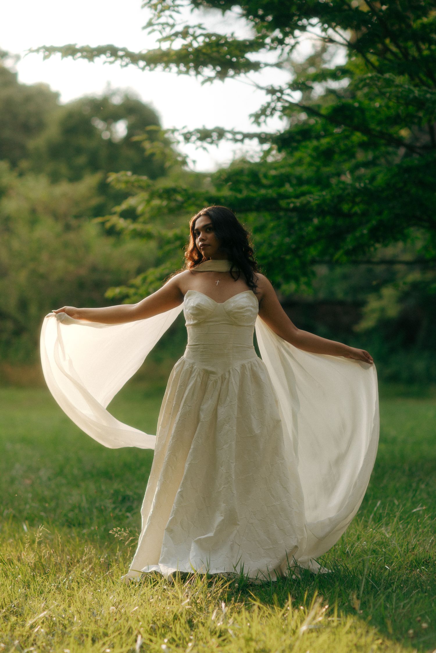 Bride in flowing white strapless gown twirling in lush green garden, dress billowing gracefully in natural light.