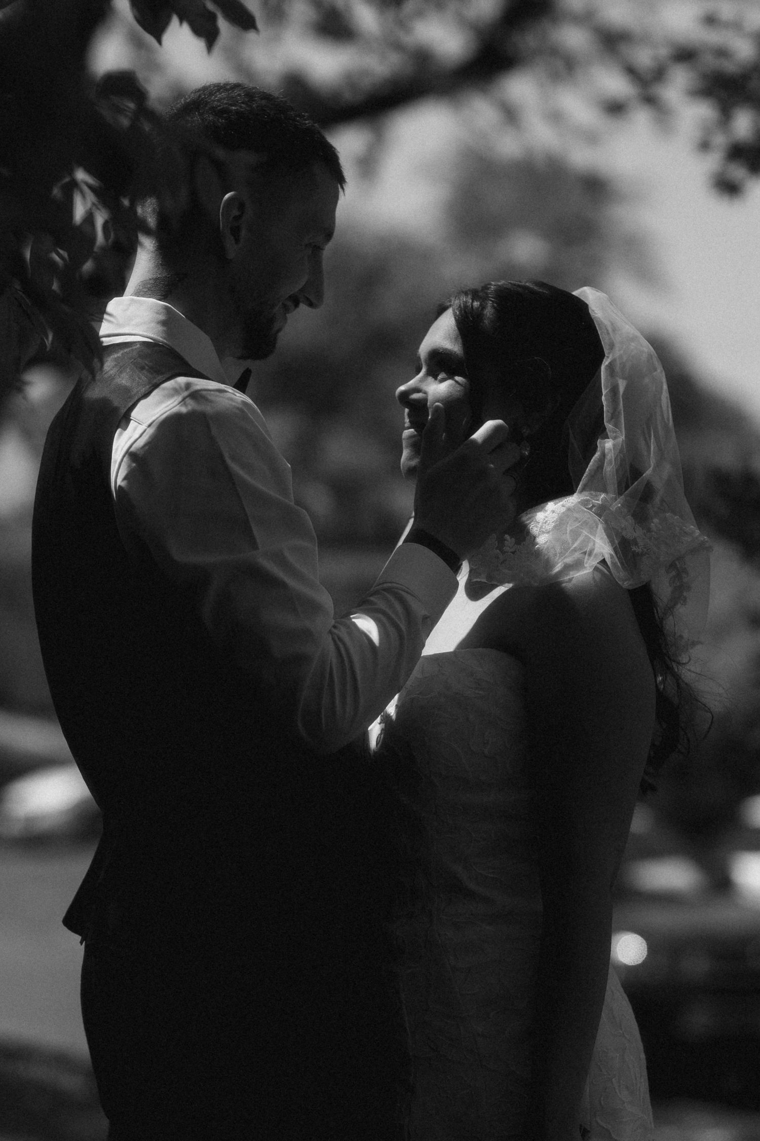 Black and white wedding photo of groom tenderly cupping brides face as they share an intimate moment outdoors.