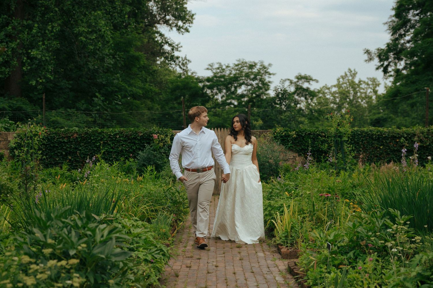 Bride and groom walking hand in hand through a lush garden path on their wedding day.