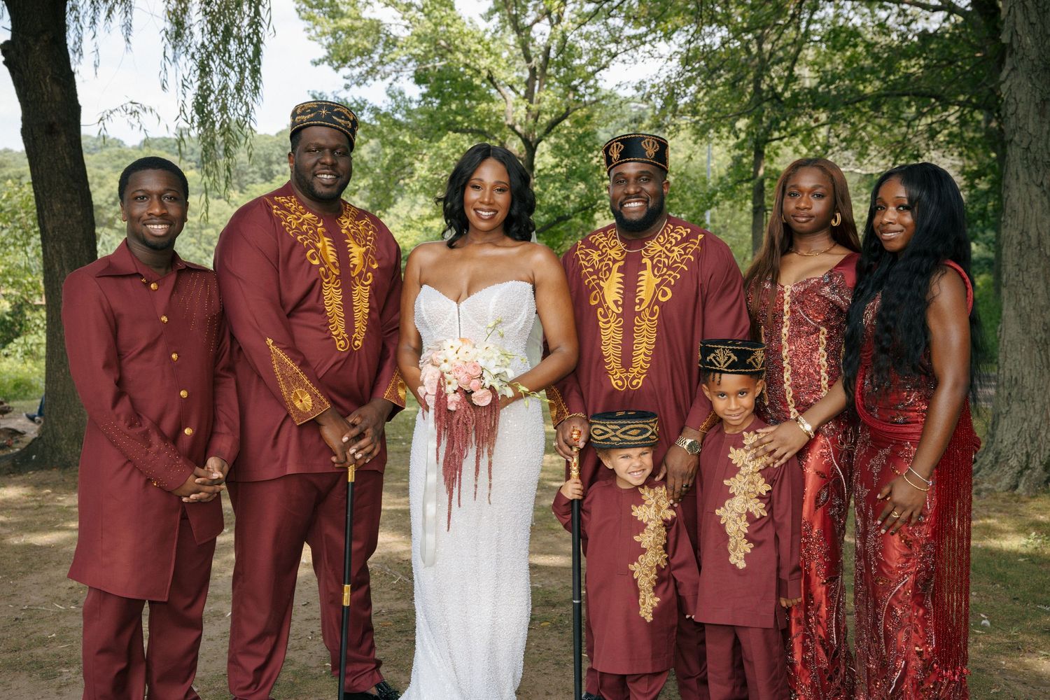 Wedding party in matching burgundy and gold African traditional attire with bride in white.