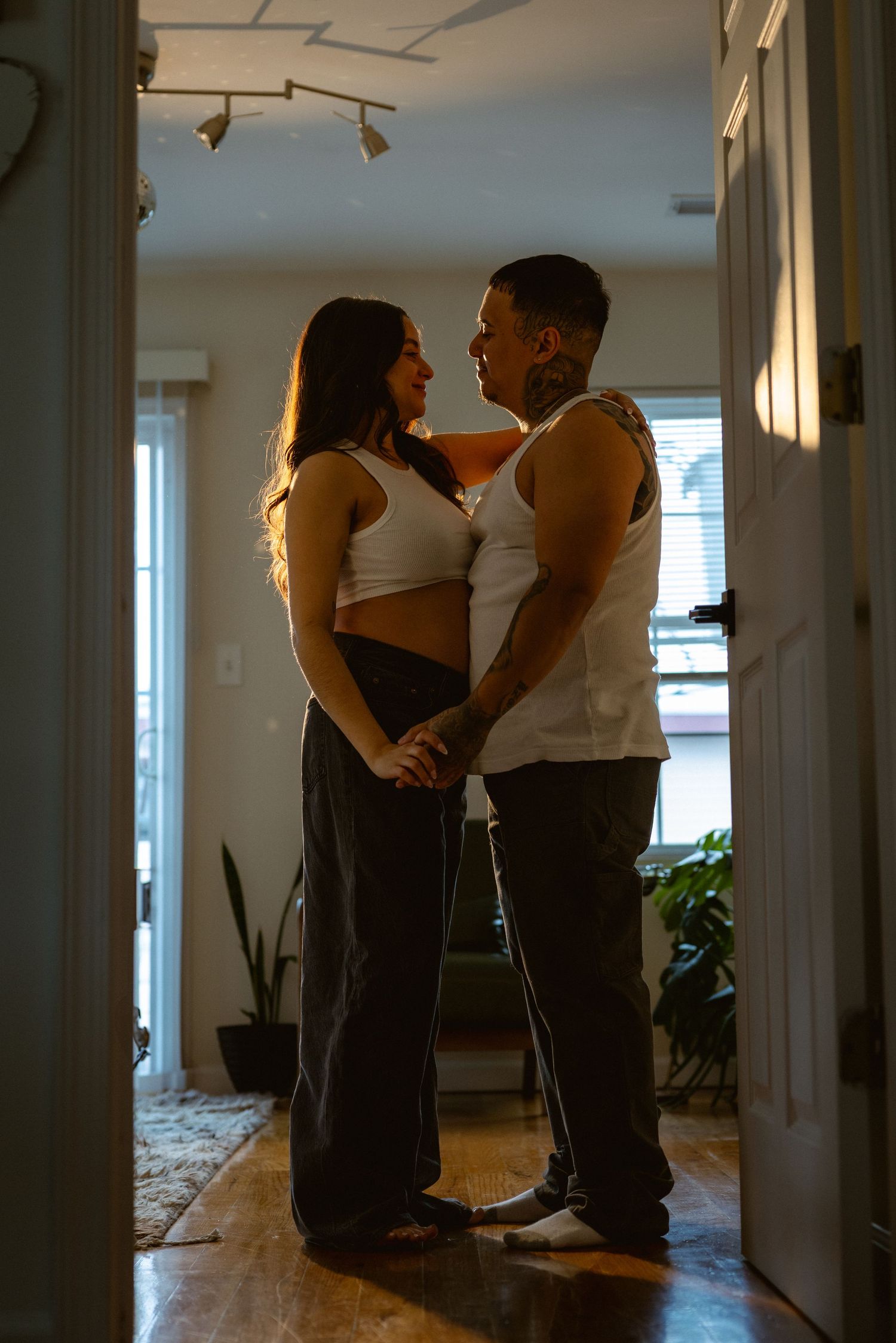 Couple holding hands and gazing at each other lovingly in a warmly lit home hallway.