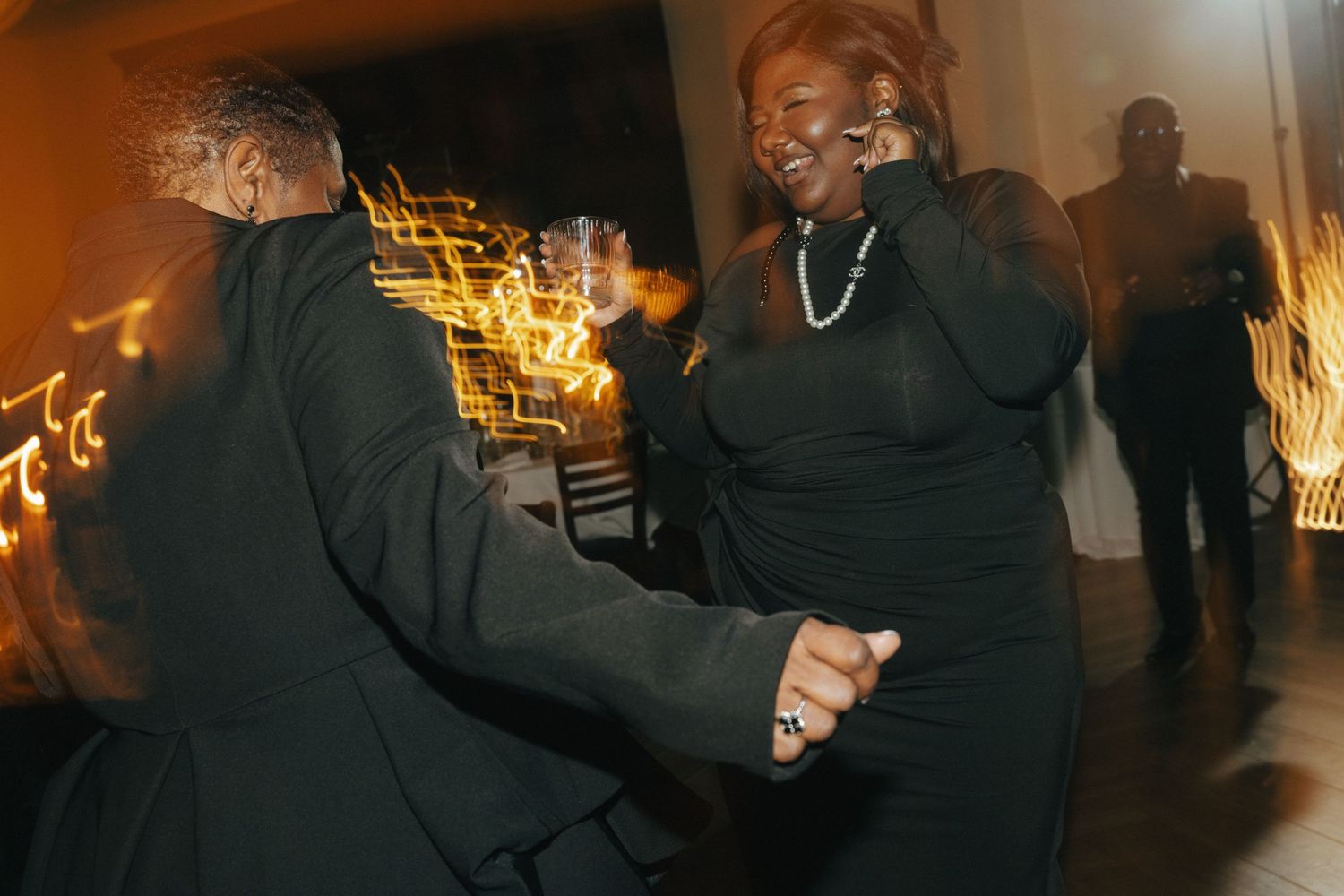 Guests in black attire dancing joyfully at an elegant evening wedding reception.
