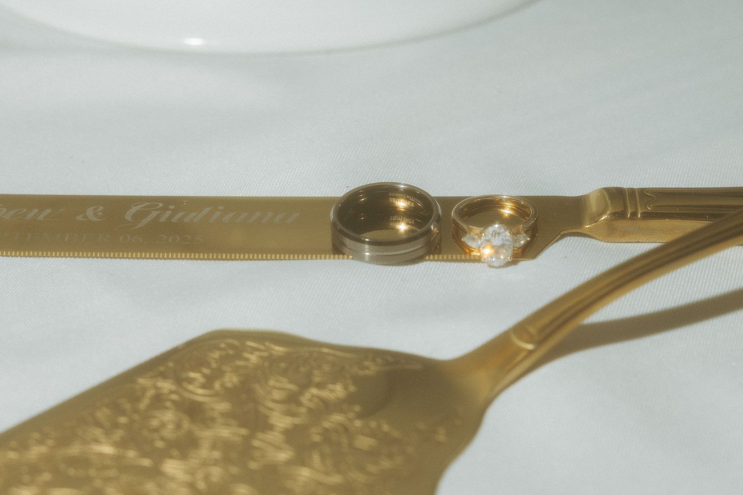 Gold engraved wedding cake serving set with bride and groom rings displayed on white tablecloth.