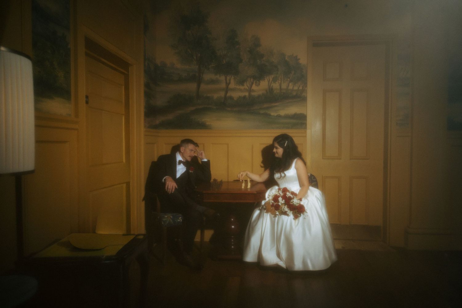Bride and groom share intimate moment at small table in warmly lit vintage room.