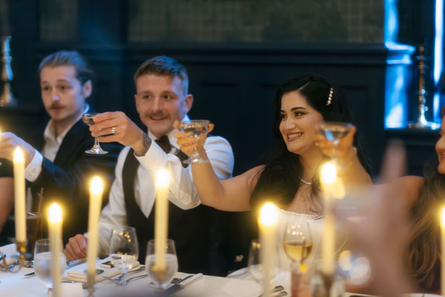 Bride and groom raise glasses in a candlelit toast at their wedding reception dinner table.