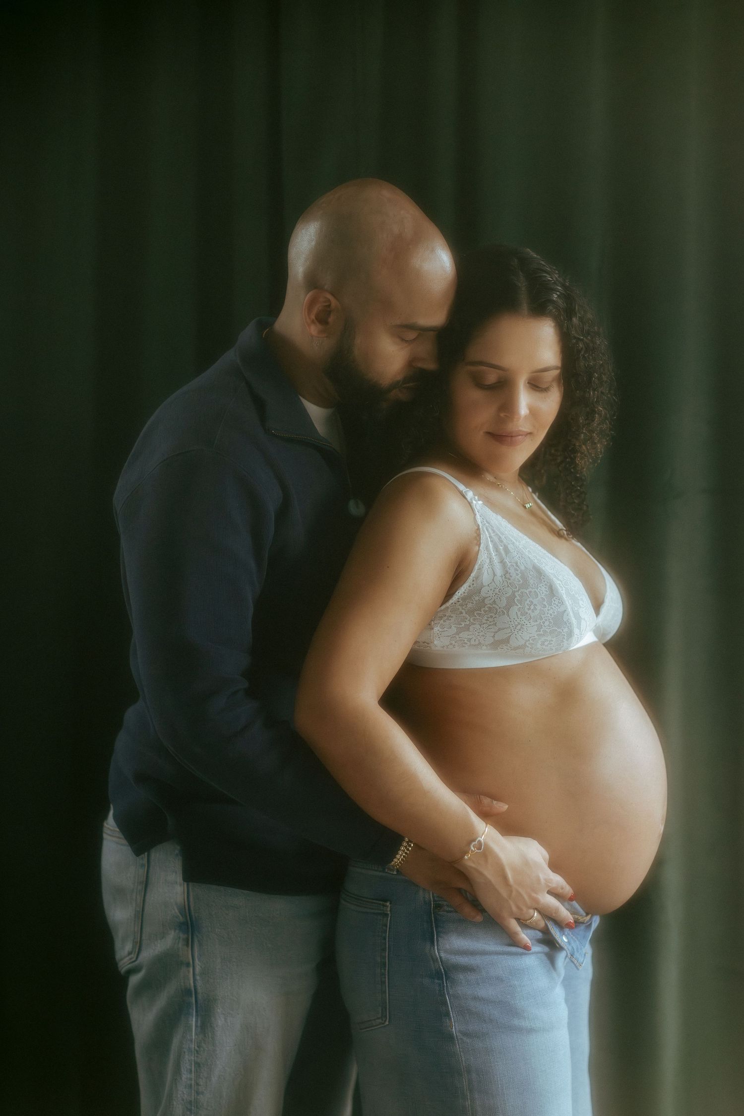 Couple sharing tender maternity moment, man embracing pregnant woman from behind, studio portrait.