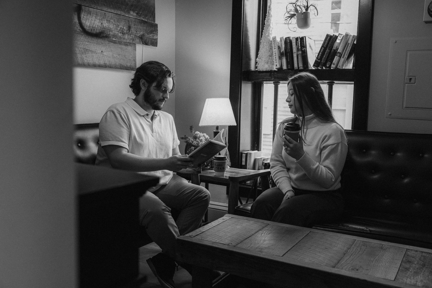 Black and white photo of a man and woman sitting together in a cozy room, reading and relaxing on leather furniture.