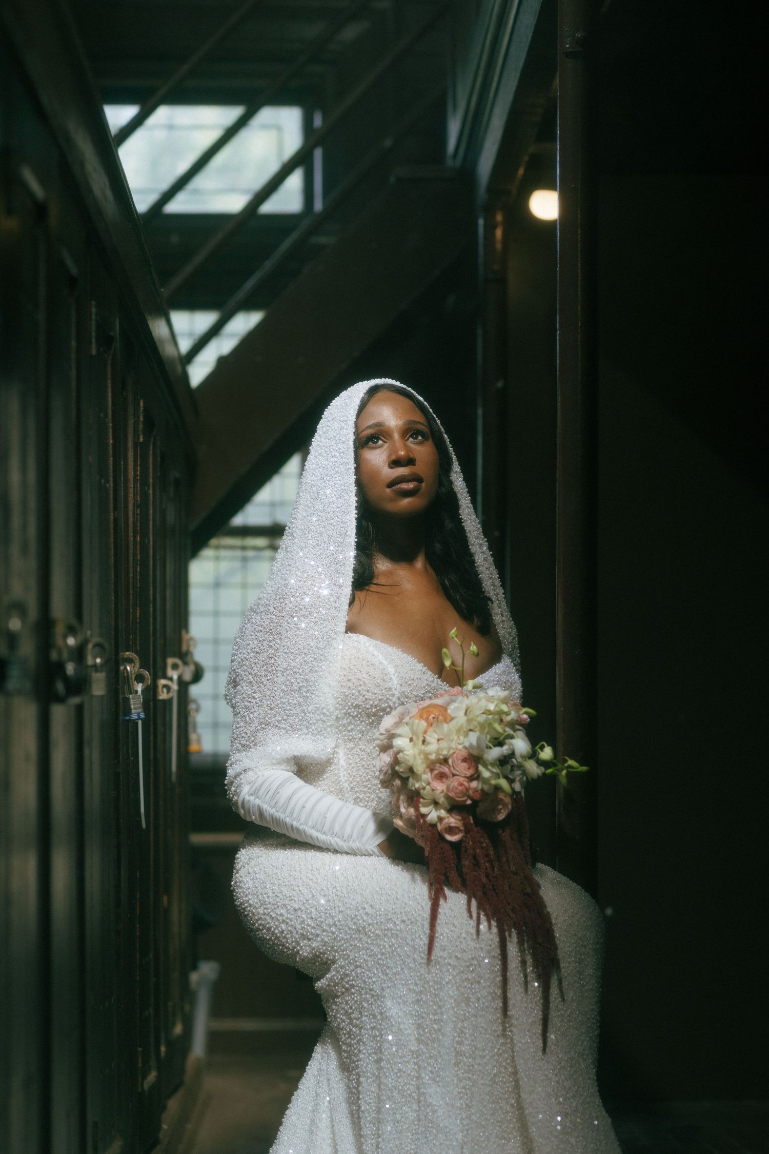 Bride in sparkle gown and white veil holding bouquet in moody locker room.