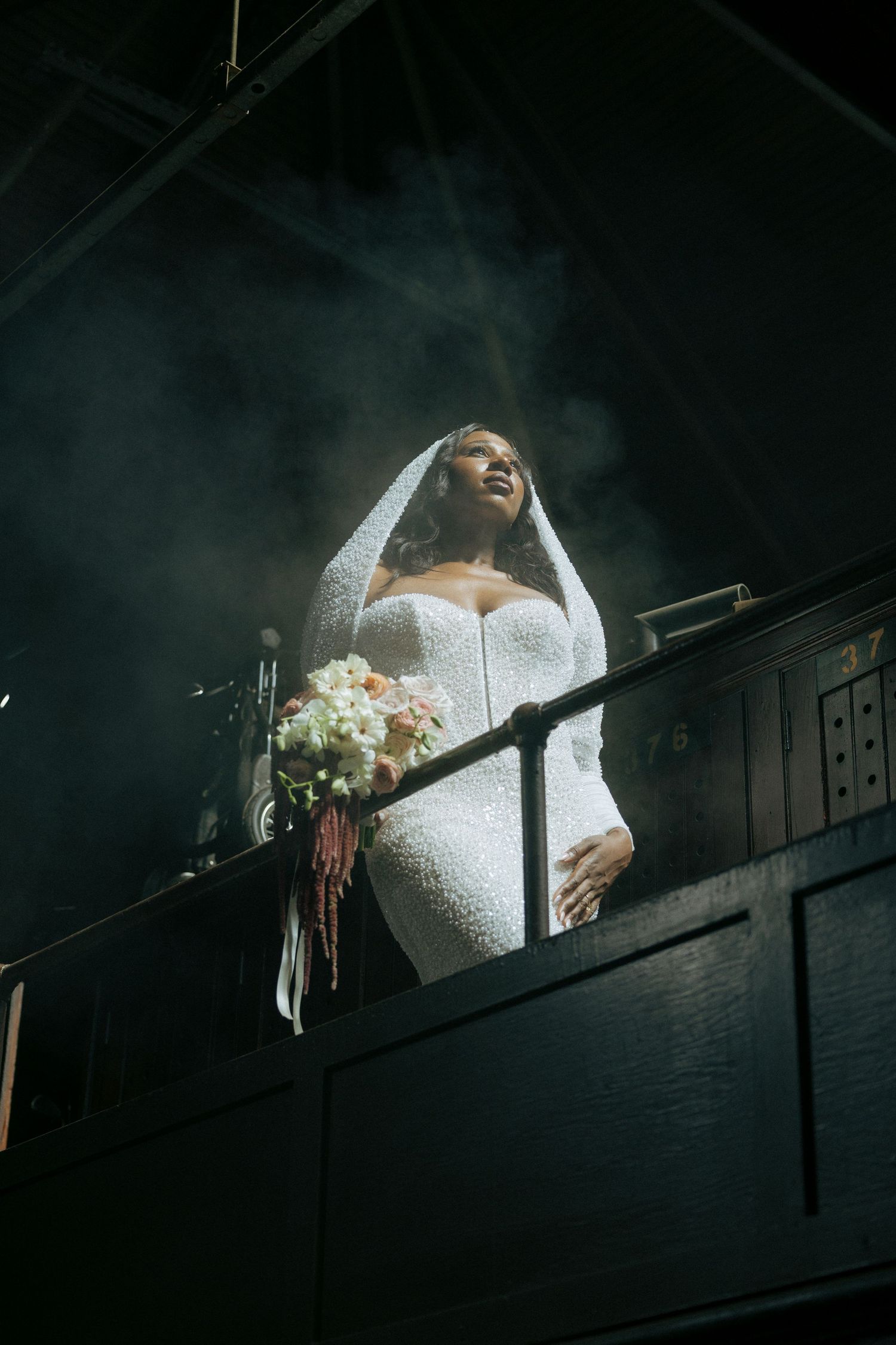 Dramatic low-angle shot of bride on balcony with bouquet surrounded by atmospheric smoke.